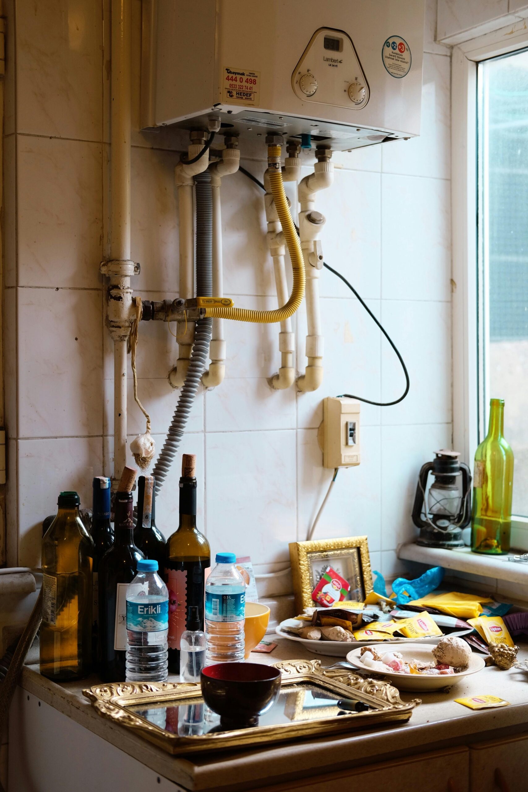 A cluttered kitchen counter with various bottles, food items, and kitchen equipment creating a messy appearance.